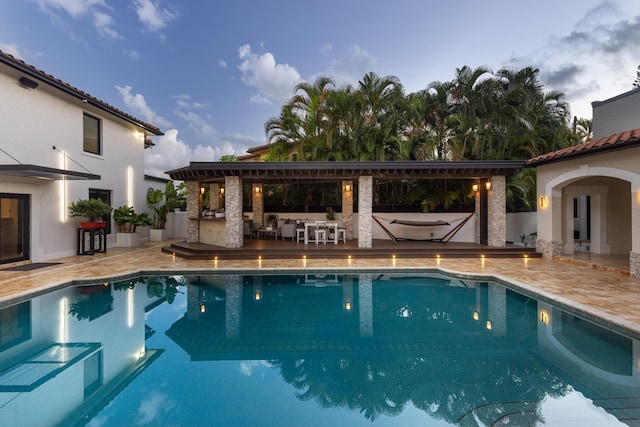 pool at dusk featuring a patio and an outdoor kitchen