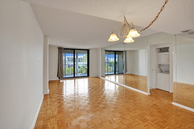 unfurnished room featuring stacked washer and dryer, light parquet floors, an inviting chandelier, and a textured ceiling