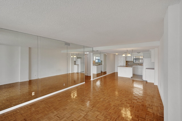 unfurnished living room featuring parquet floors, a chandelier, and a textured ceiling