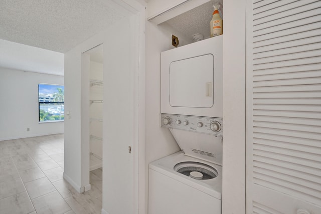 washroom featuring stacked washing maching and dryer, light tile patterned floors, and a textured ceiling