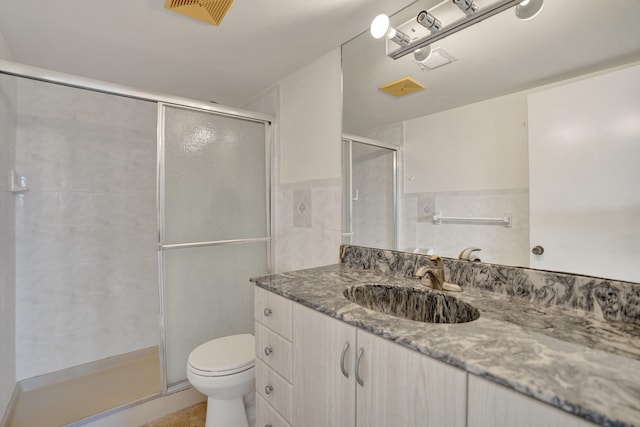 bathroom with vanity, tile walls, toilet, and a shower with door