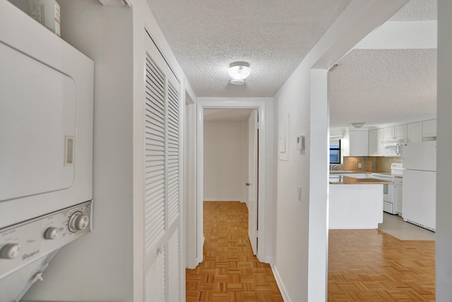 hallway featuring stacked washer and clothes dryer, light parquet flooring, and a textured ceiling