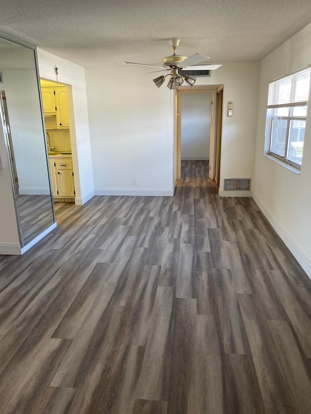 interior space with ceiling fan, a textured ceiling, and dark wood-type flooring