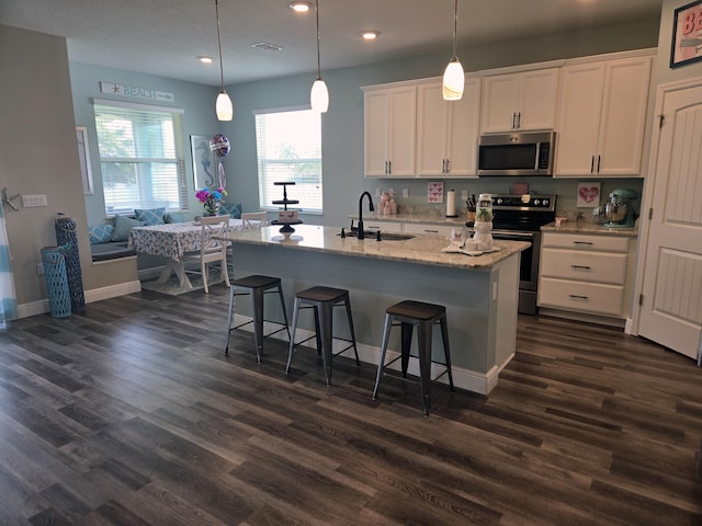 kitchen with dark wood-type flooring, a center island with sink, sink, white cabinets, and appliances with stainless steel finishes