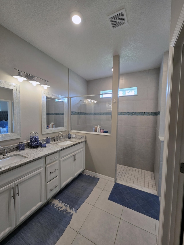 bathroom featuring a tile shower, tile patterned flooring, vanity, and a textured ceiling