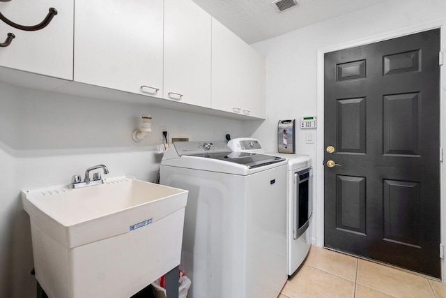 washroom with light tile patterned floors, sink, a textured ceiling, cabinets, and washing machine and dryer