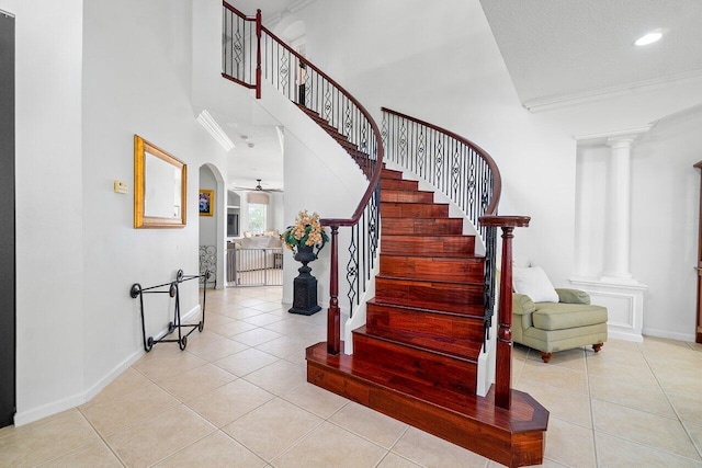 stairs featuring ceiling fan, ornamental molding, decorative columns, a towering ceiling, and tile patterned flooring