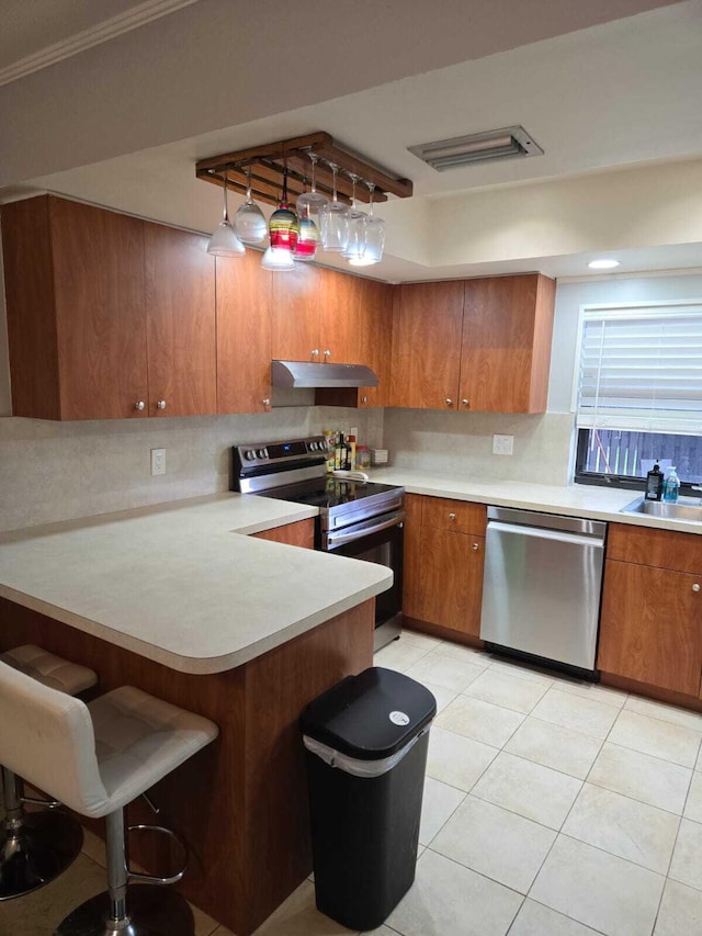 kitchen with appliances with stainless steel finishes, sink, kitchen peninsula, ornamental molding, and light tile patterned floors