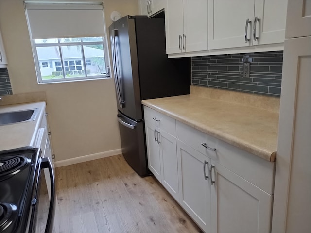 kitchen featuring light wood-type flooring, sink, white cabinetry, stainless steel range, and backsplash