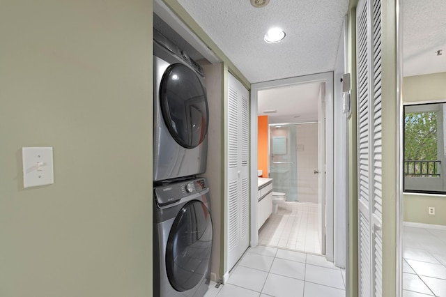 clothes washing area with stacked washer / dryer, a textured ceiling, and light tile patterned flooring