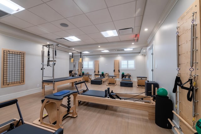 workout room with a paneled ceiling, ornamental molding, and light hardwood / wood-style flooring