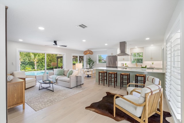 living room with ceiling fan, plenty of natural light, sink, and light hardwood / wood-style floors