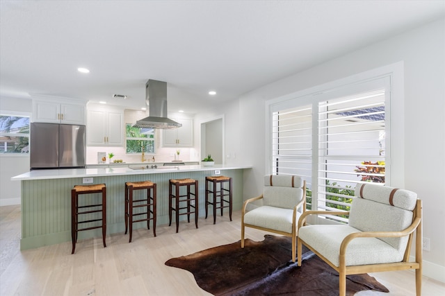 kitchen with white cabinetry, island exhaust hood, stainless steel fridge, and kitchen peninsula