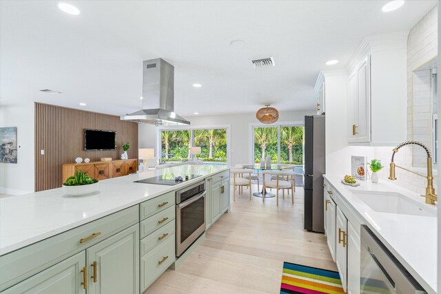 kitchen featuring appliances with stainless steel finishes, white cabinets, wall chimney range hood, sink, and backsplash