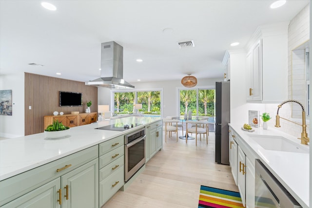 kitchen featuring appliances with stainless steel finishes, tasteful backsplash, sink, island exhaust hood, and light wood-type flooring