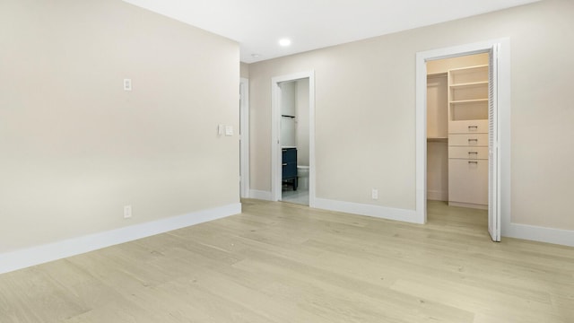 unfurnished bedroom with a walk in closet, ensuite bath, light wood-type flooring, and a closet