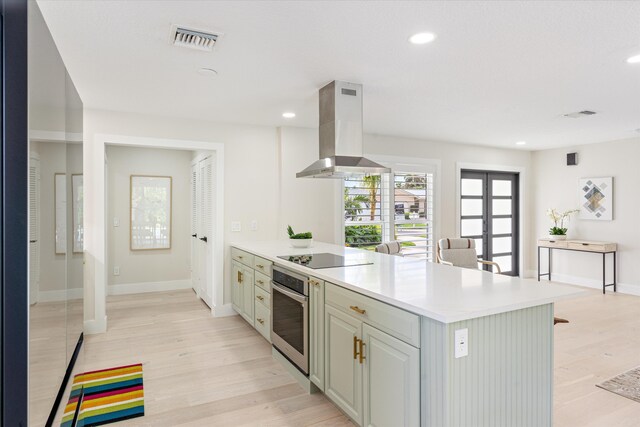 kitchen with white cabinets, a kitchen bar, island exhaust hood, stainless steel refrigerator, and light hardwood / wood-style flooring