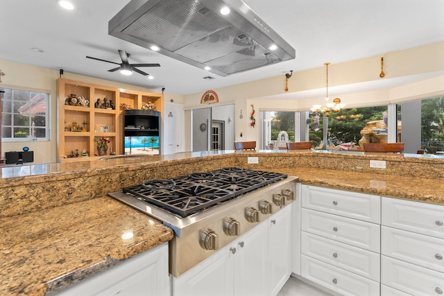 kitchen featuring ceiling fan with notable chandelier, island exhaust hood, white cabinets, dark stone countertops, and stainless steel gas stovetop