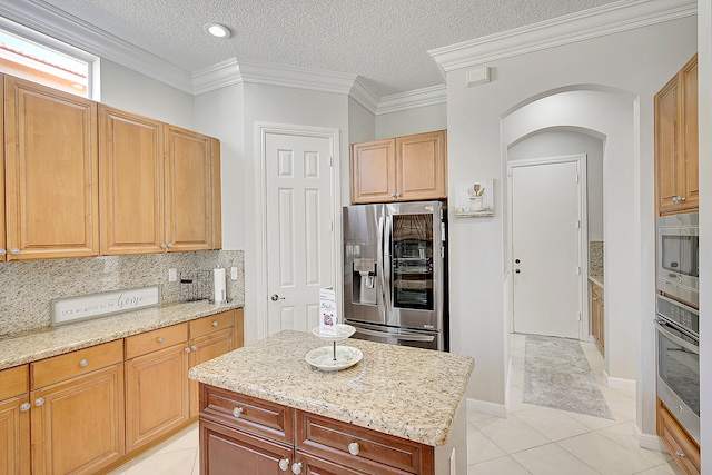 kitchen with light tile patterned floors, appliances with stainless steel finishes, a kitchen island, a textured ceiling, and crown molding