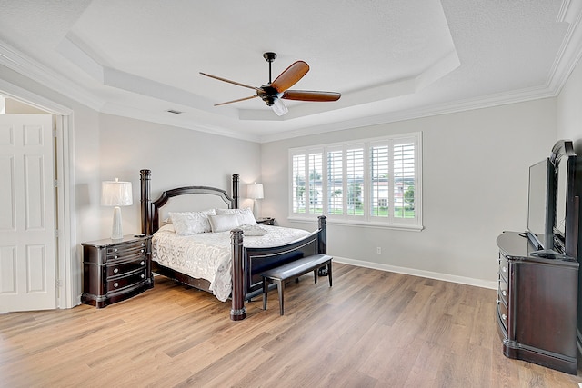 bedroom with ceiling fan, ornamental molding, a tray ceiling, and light wood-type flooring