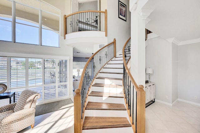 stairway featuring a towering ceiling, crown molding, and decorative columns