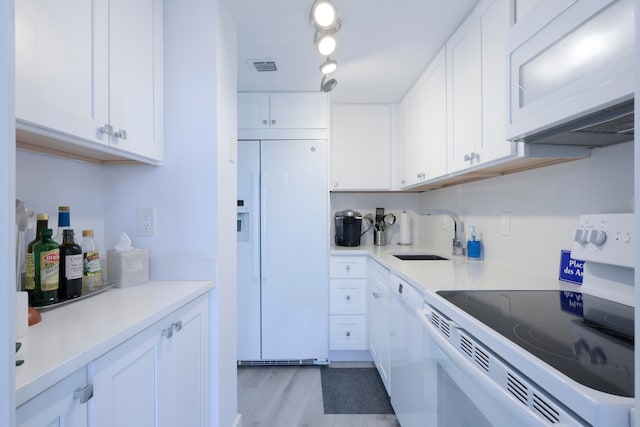 kitchen with white appliances, light hardwood / wood-style flooring, sink, and white cabinets