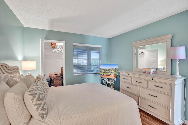 bedroom featuring a textured ceiling, a closet, light hardwood / wood-style floors, and a walk in closet