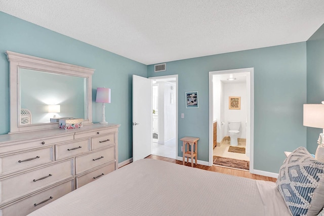 bedroom featuring a textured ceiling, light wood-type flooring, and connected bathroom