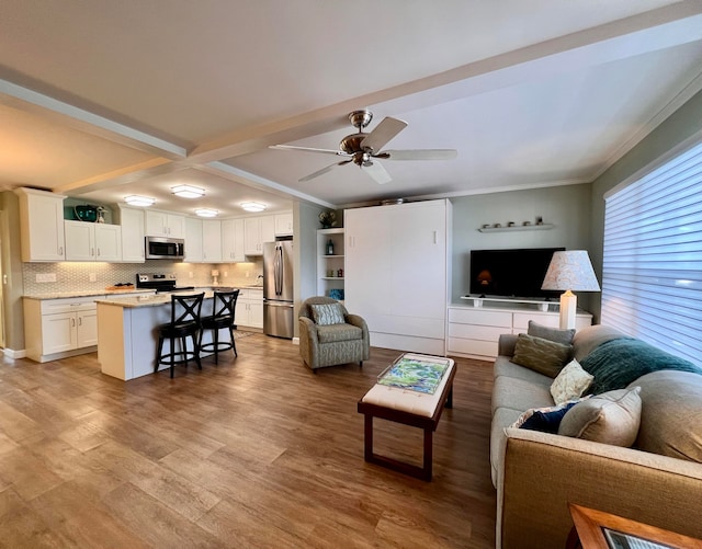 living room with ornamental molding, beamed ceiling, light wood-type flooring, and ceiling fan