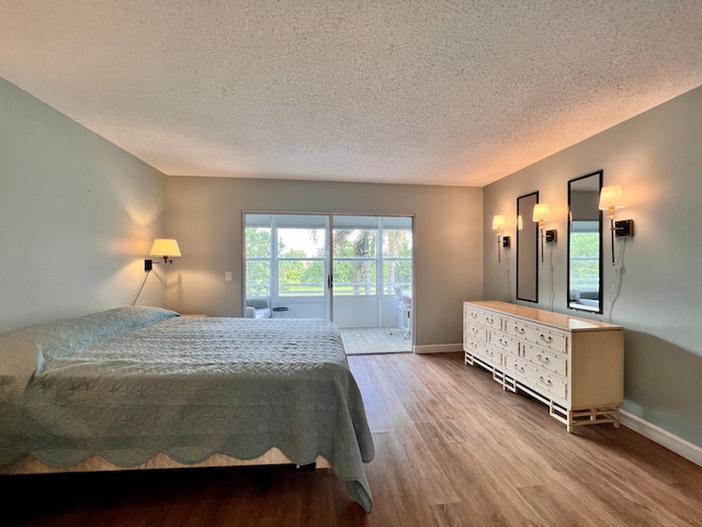 bedroom with access to outside, hardwood / wood-style floors, and a textured ceiling