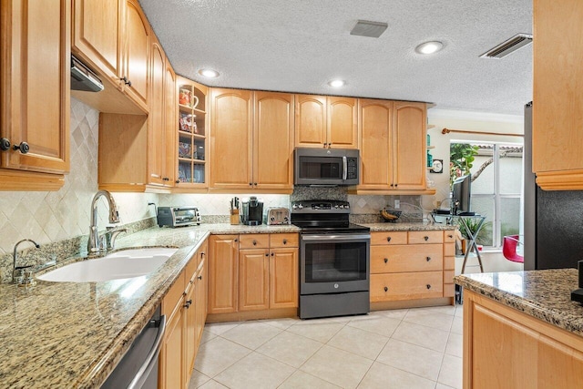 kitchen with light stone countertops, light tile patterned flooring, appliances with stainless steel finishes, and sink