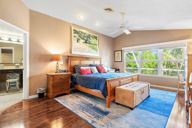 bedroom with ceiling fan, a textured ceiling, vaulted ceiling, ensuite bathroom, and dark wood-type flooring