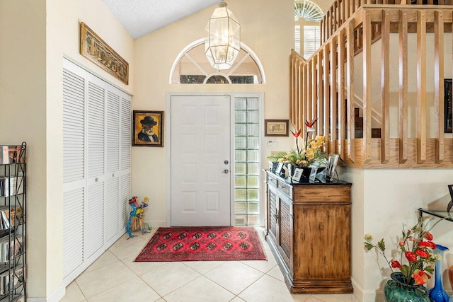 tiled entryway featuring a textured ceiling, vaulted ceiling, and a chandelier