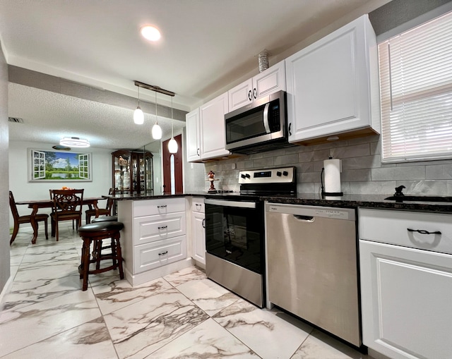 kitchen featuring white cabinets, pendant lighting, kitchen peninsula, backsplash, and stainless steel appliances