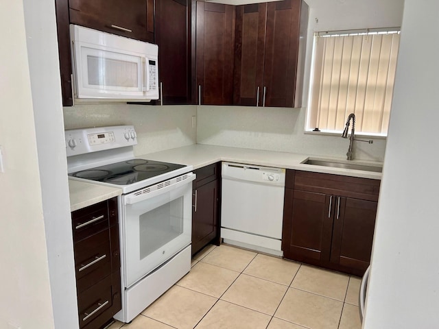 kitchen with dark brown cabinetry, sink, light tile patterned flooring, and white appliances