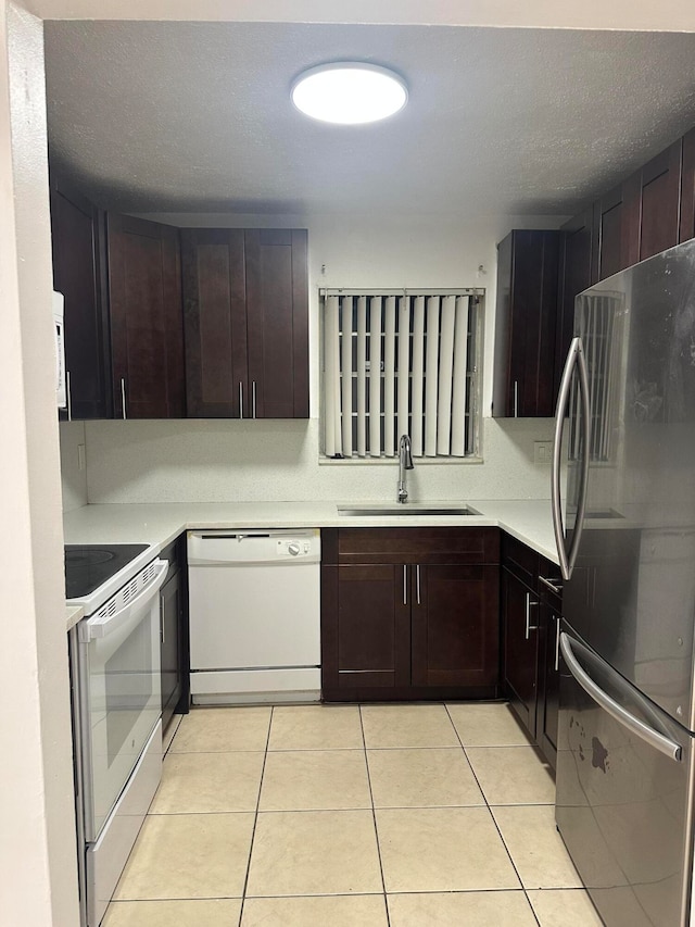 kitchen with dark brown cabinets, white appliances, a textured ceiling, sink, and light tile patterned floors