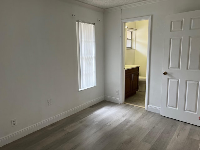 unfurnished bedroom featuring light hardwood / wood-style floors, ornamental molding, a textured ceiling, and connected bathroom