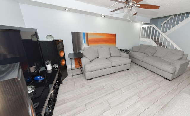 living room with light wood-type flooring, ceiling fan, and a textured ceiling