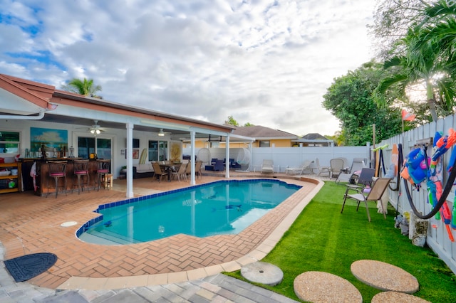 view of pool with a yard, ceiling fan, a bar, and a patio