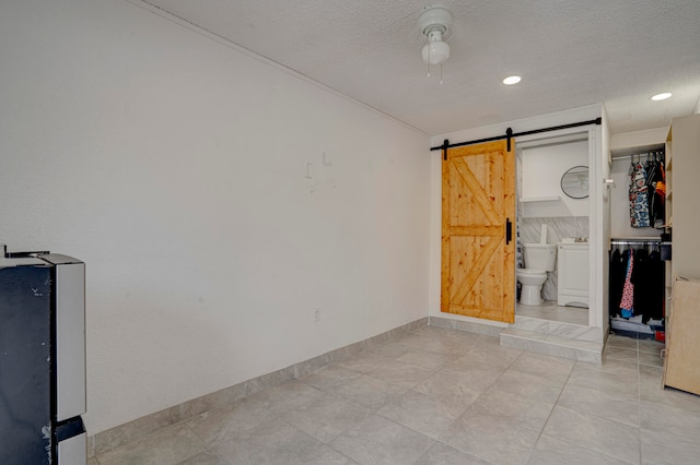 unfurnished bedroom with ceiling fan, connected bathroom, a barn door, light tile patterned floors, and a textured ceiling