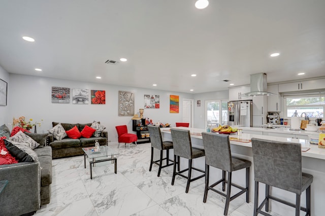 kitchen with white cabinets, stainless steel fridge with ice dispenser, a kitchen bar, and island range hood