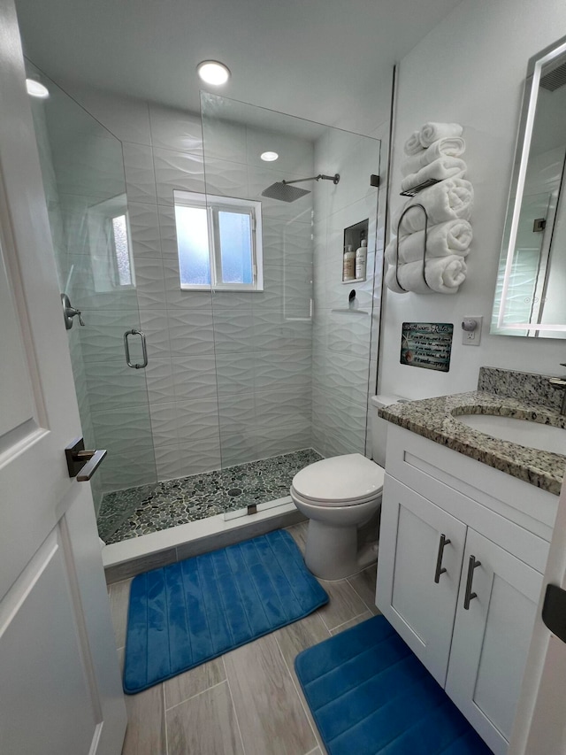 bathroom featuring vanity, a shower with door, and toilet