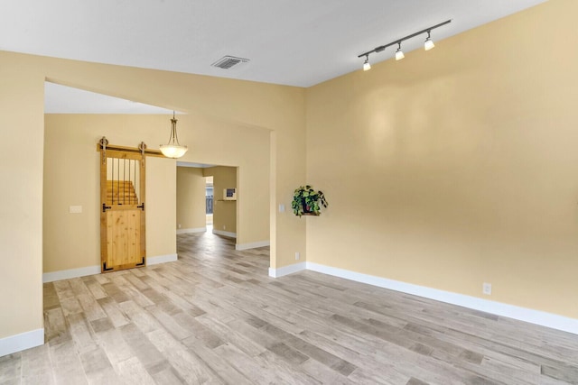 empty room with light hardwood / wood-style floors, a barn door, rail lighting, and vaulted ceiling