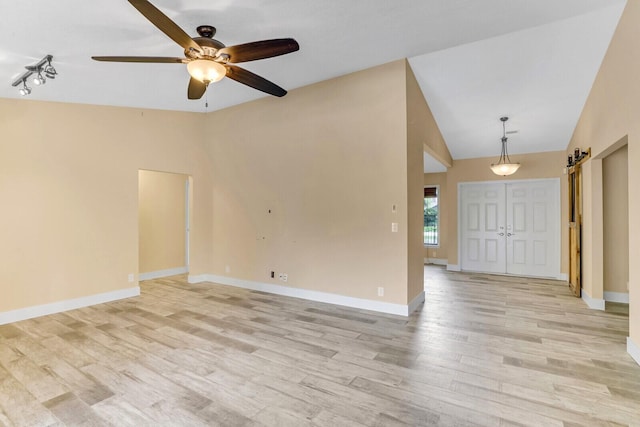 unfurnished room featuring a barn door, light hardwood / wood-style floors, ceiling fan, and lofted ceiling