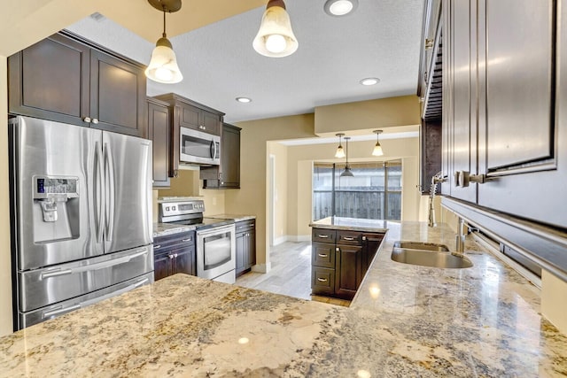 kitchen with pendant lighting, stainless steel appliances, light stone counters, and dark brown cabinets