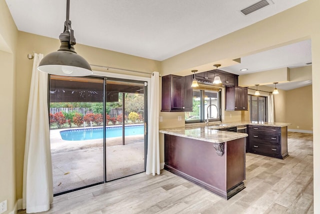 kitchen featuring pendant lighting, sink, light hardwood / wood-style flooring, light stone countertops, and kitchen peninsula