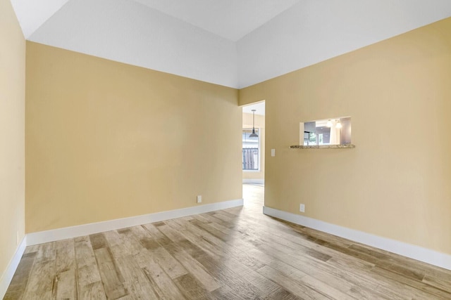 spare room featuring light wood-type flooring and vaulted ceiling