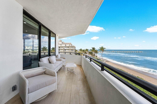 balcony featuring an outdoor hangout area, a water view, and a beach view