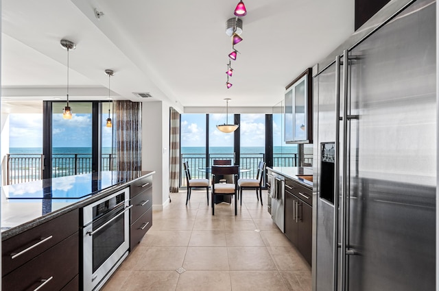 kitchen with a water view, appliances with stainless steel finishes, decorative light fixtures, and dark brown cabinetry