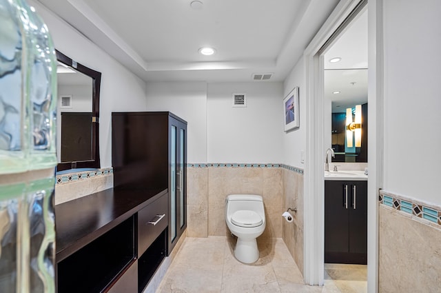 bathroom with toilet, vanity, a tray ceiling, and tile walls